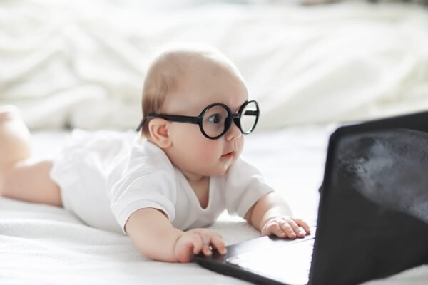 A newborn baby is lying on a soft bed in glasses. bébé avec des lunettes qui utilise un ordinateur portable
